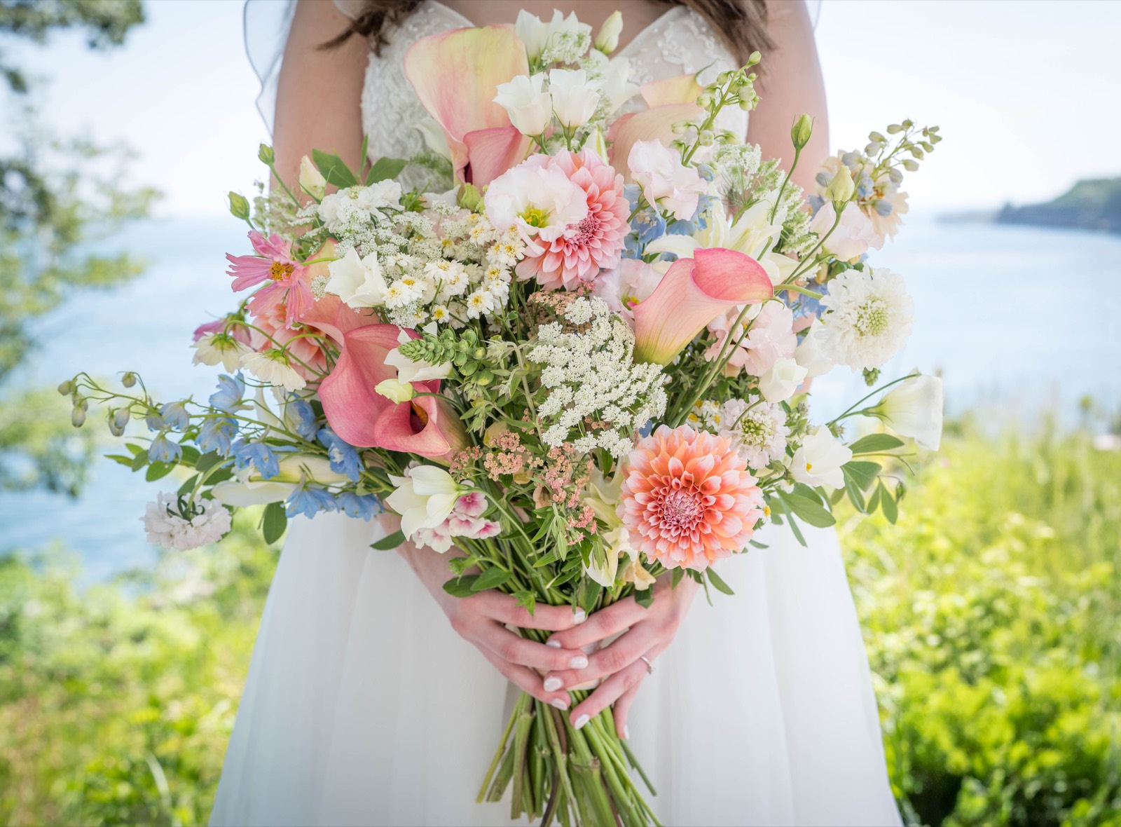 Pastel bridal bouquet of dahlias, callas and sweet peas, the sea behind
