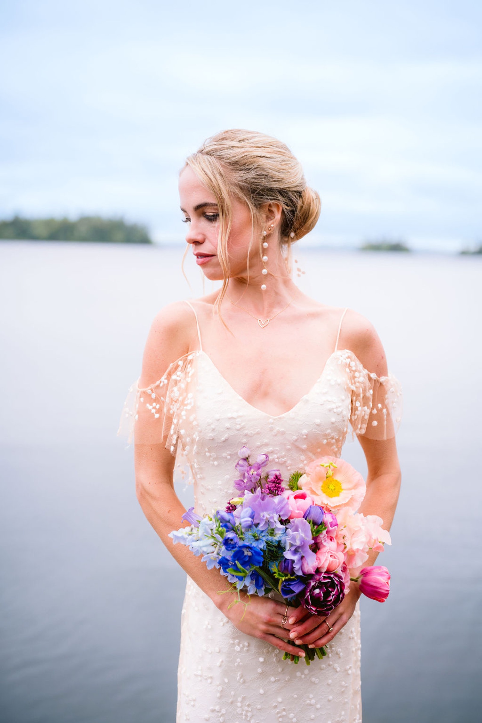 Bride at the water's edge carrying a pastel farm-grown bouquet