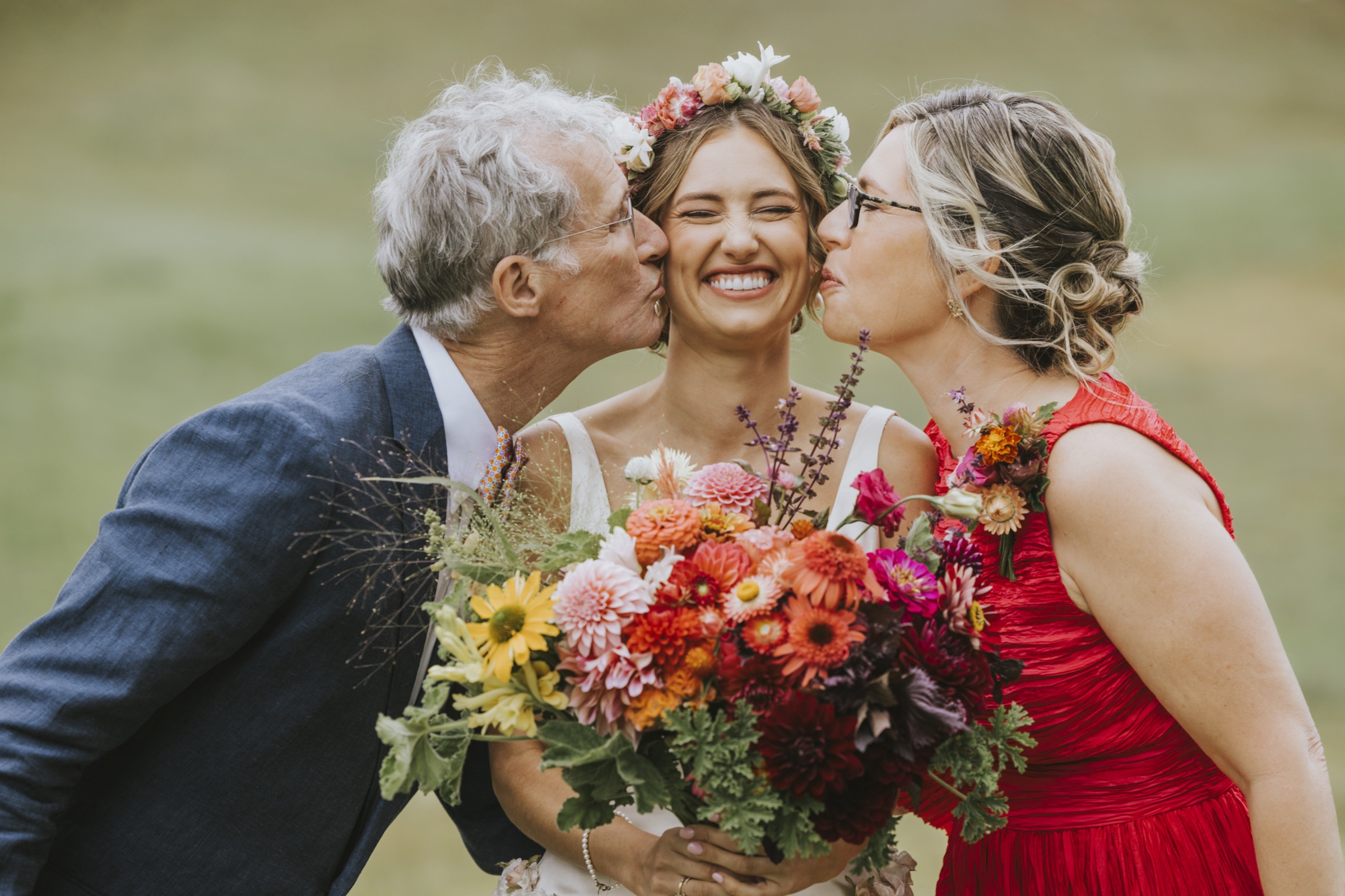 Parents kissing the bride, her bouquet of vivid orange farm blooms in hand