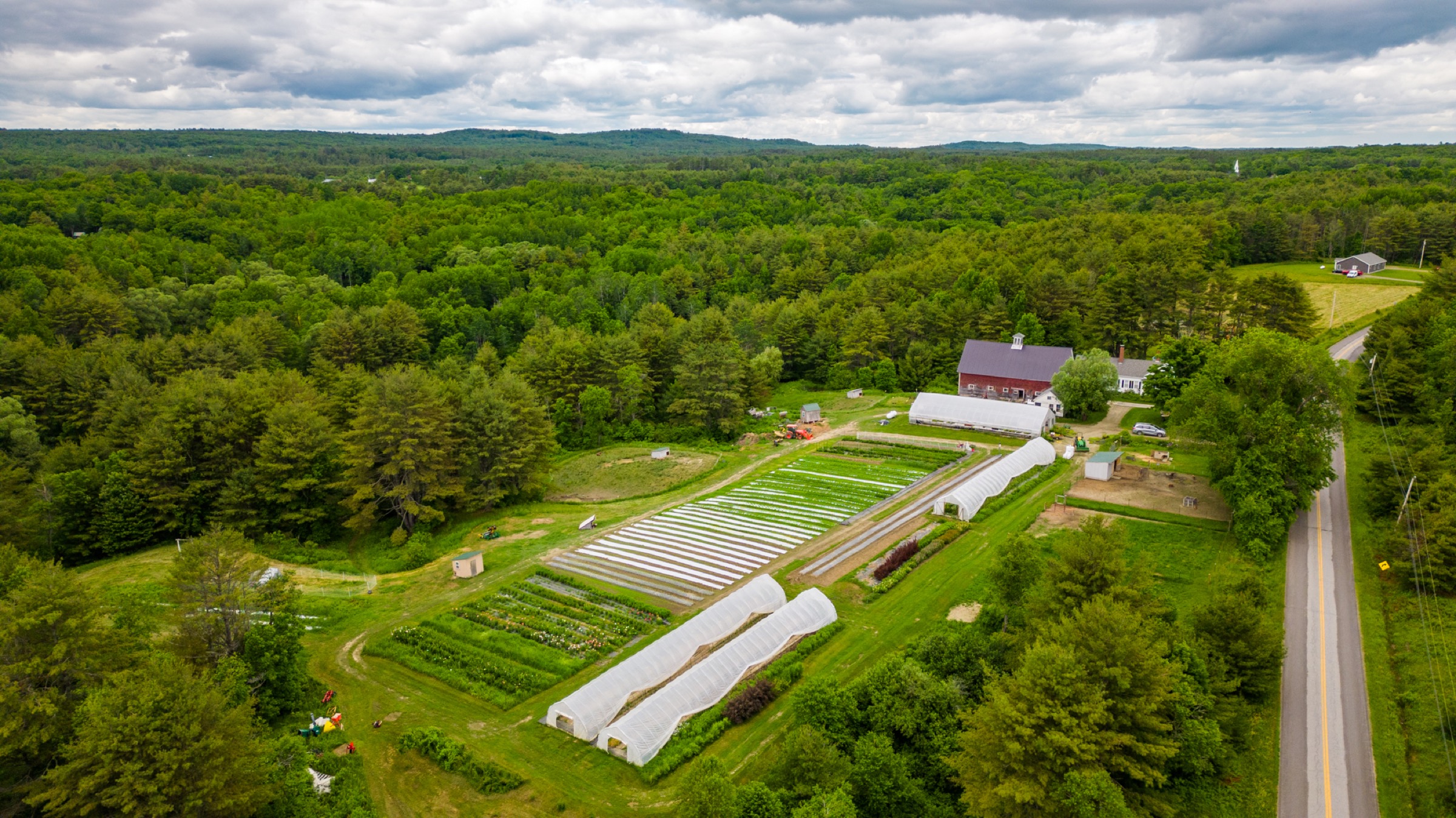The farm from above — greenhouses, rows and the barn among the trees