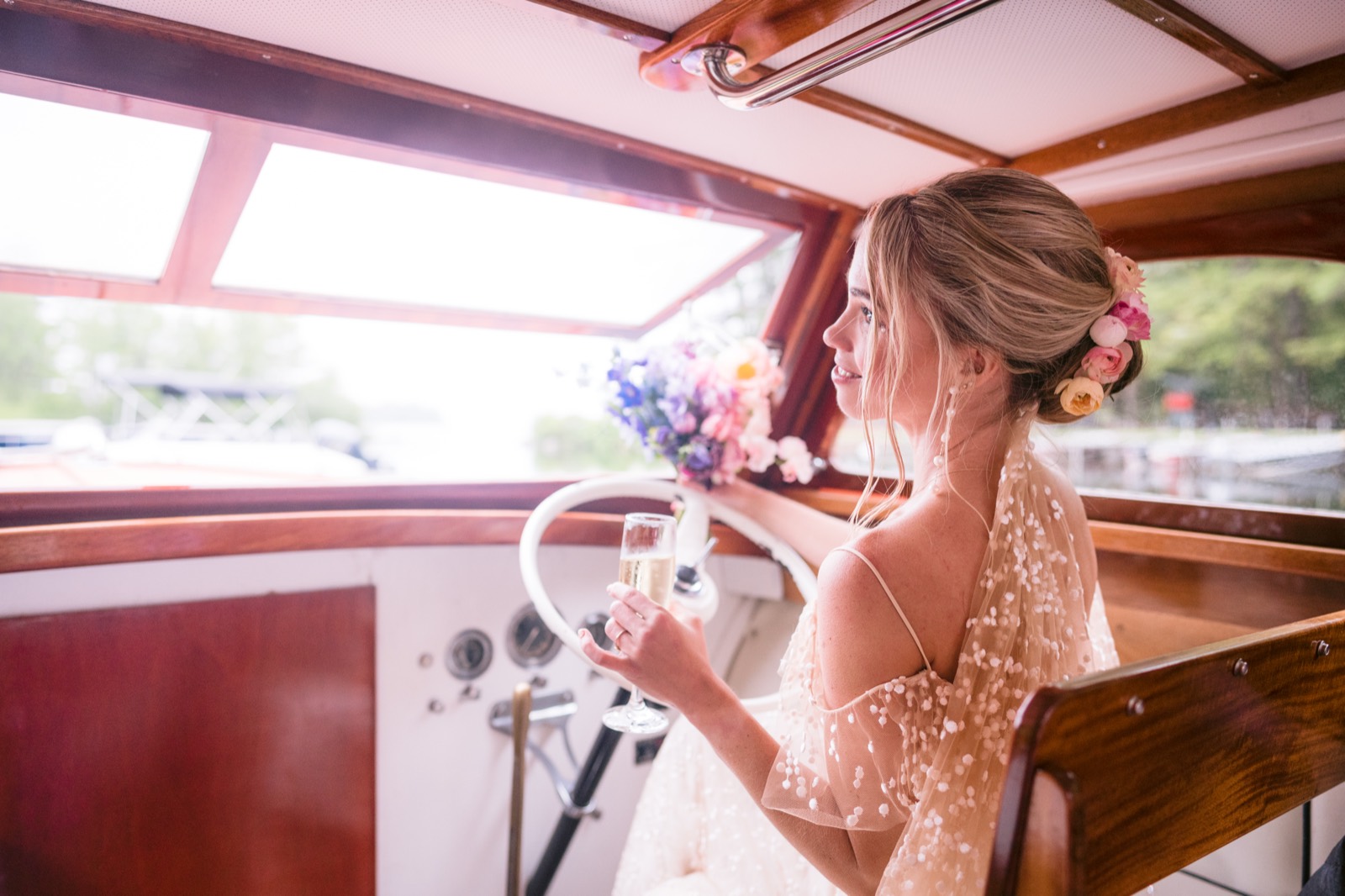 Bride at the helm of a wooden boat, bouquet in hand