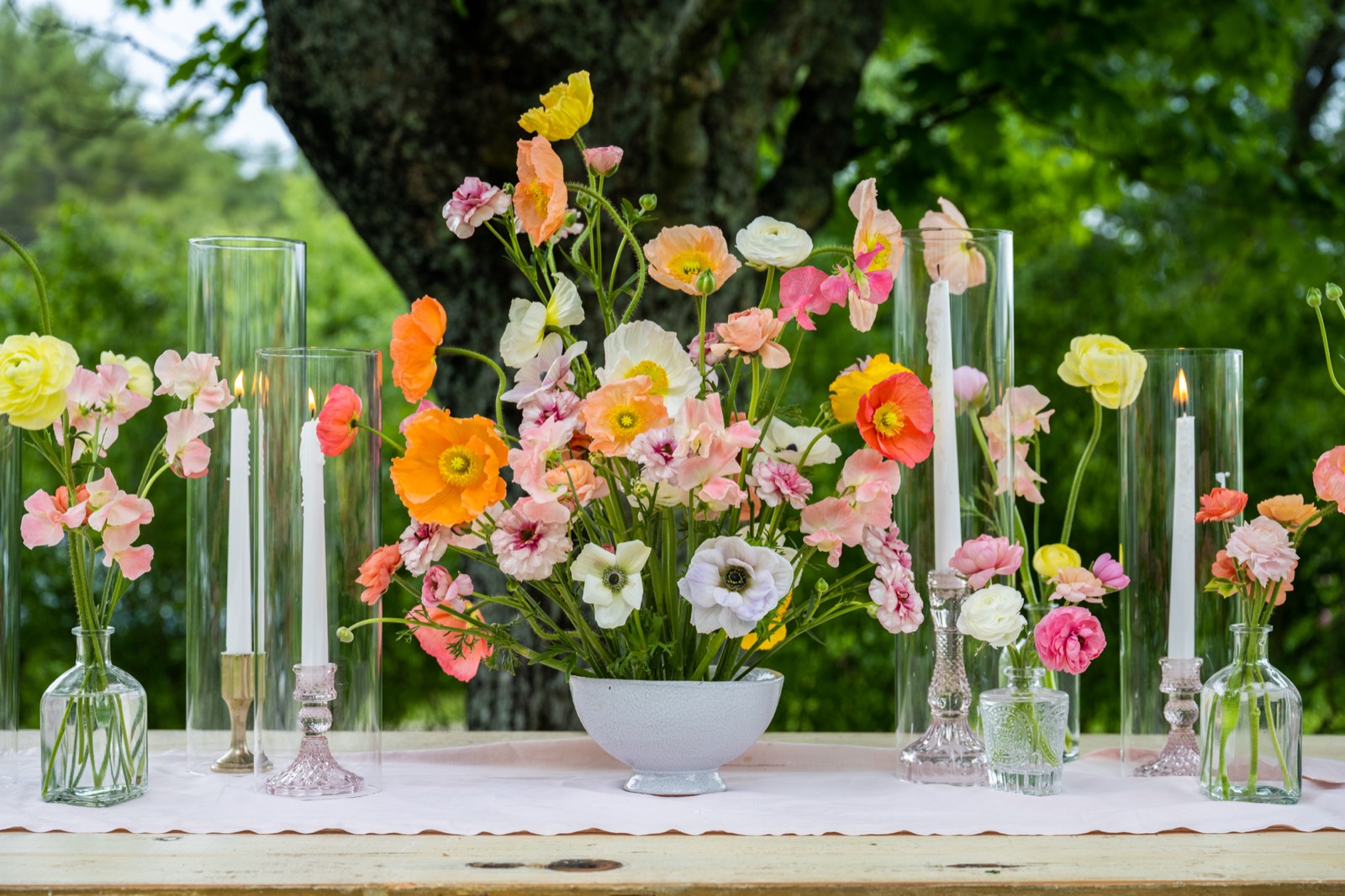 Poppy and ranunculus centerpiece styled in its vase among taper candles